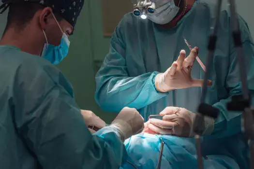 closeup of two surgeons in scrubs and surgical gear performing penis enlargement surgery