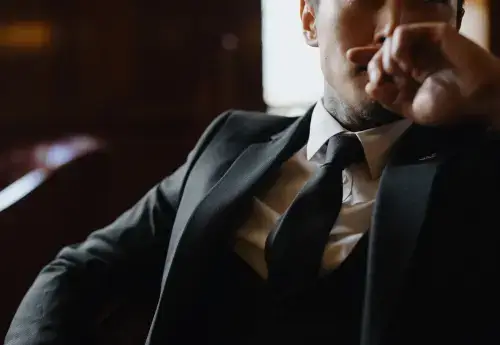 Closeup of a dark skinned man in a nice suit and tie sitting in a dark leather chair with his chin resting on his hand
