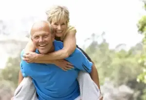 a happy older couple laughs as the man carries the woman on his back