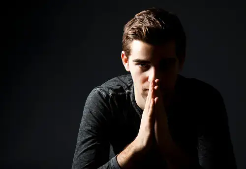a handsome man's face against black background with dramatic lighting holds his hands to his face in a prayer symbolizing before and after a penuma implant