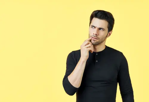Man looking thoughtful against yellow background, representing curiosity about how to measure your penis accurately and confidently.