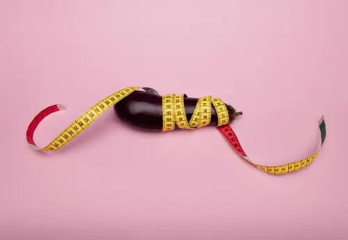 Eggplant wrapped with a measuring tape on a pink background, symbolizing how to measure your penis girth accurately at home.