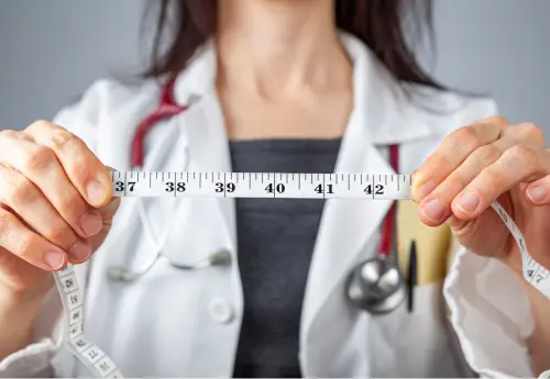 Medical professional in white coat holding measuring tape, symbolizing the importance of accurate penis measurement for personalized enhancement planning.